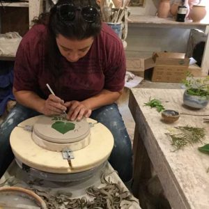 artist refines the details on the piece with a leaf pressed into it