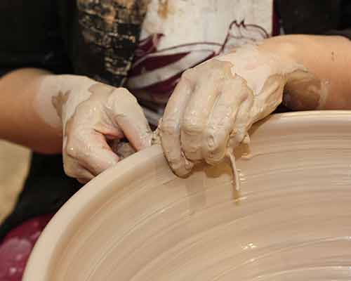 A potter is shaping the lip of a large stoneware bowl